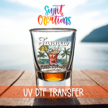 Tanned and Tipsy shot glass UV DTF transfer on a filled shot glass on a dock by the water