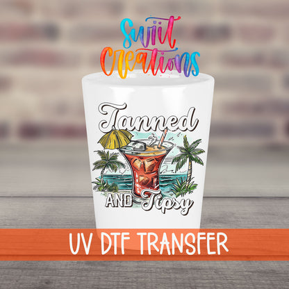 Tanned and Tipsy UV DTF transfer on a white shot glass in front of a brick wall