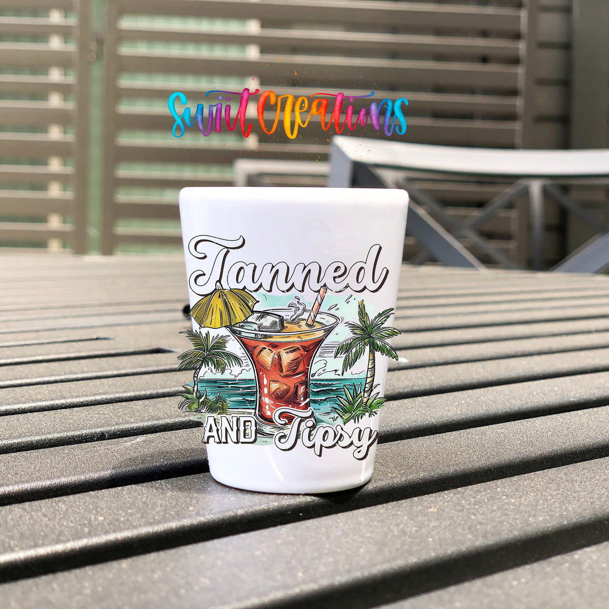 Tanned and Tipsy UV DTF transfer on a white shot glass on an outdoor patio table