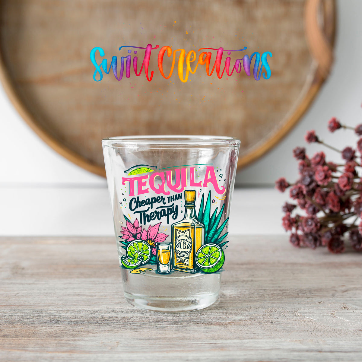 Tequila Cheaper Than Therapy shot glass transfer on a clear glass beside a wooden barrel and dried flowers