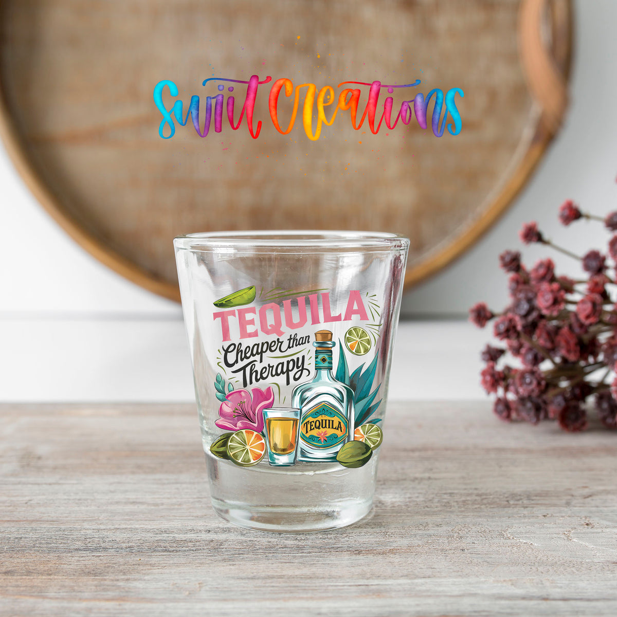 Tequila Cheaper Than Therapy shot glass transfer on a clear glass beside a wooden barrel and dried flowers