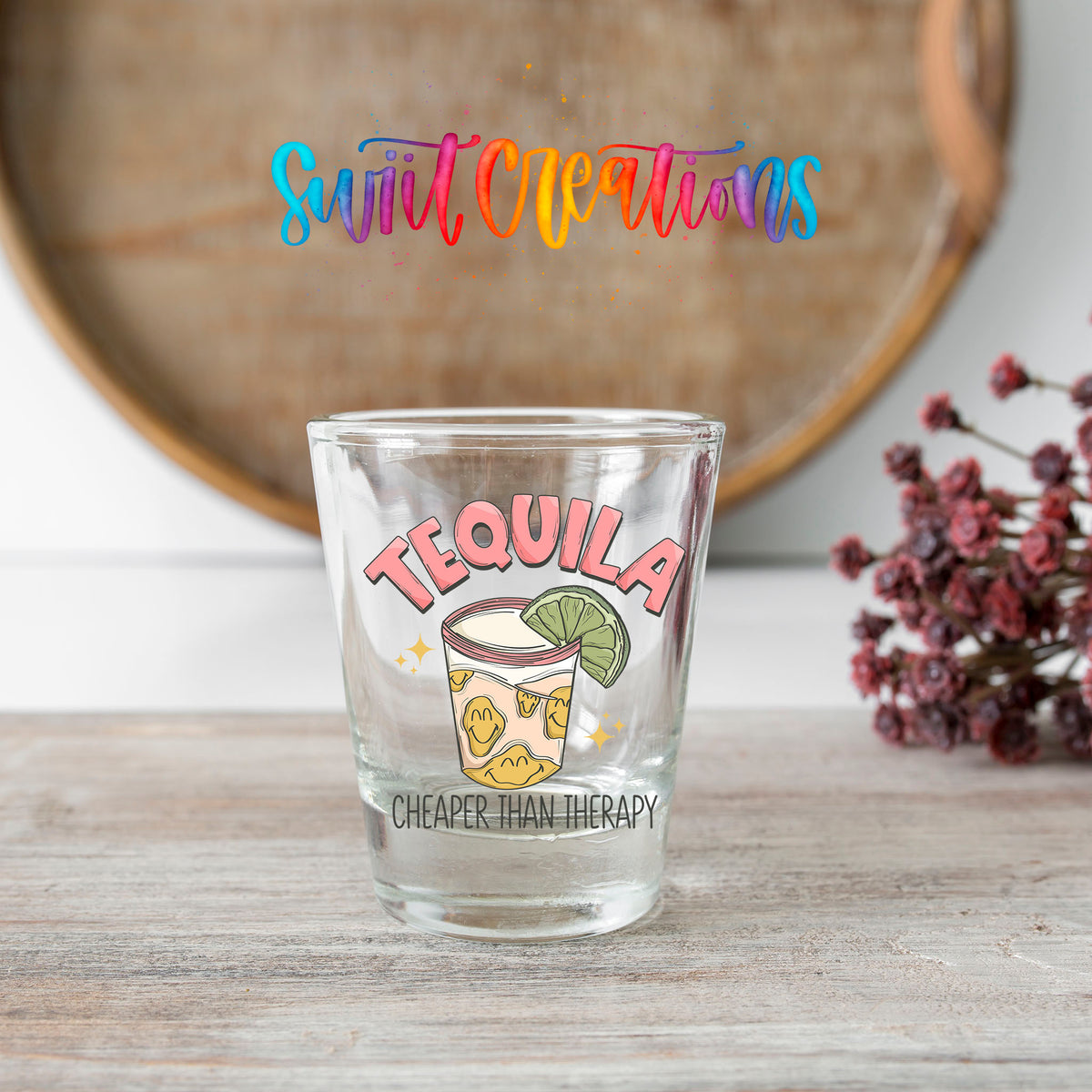 Tequila Cheaper Than Therapy shot glass transfer on a clear glass beside a wooden barrel and dried flowers