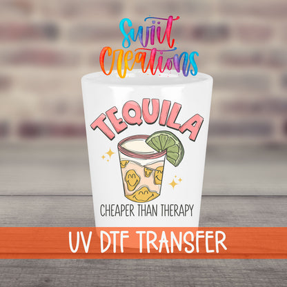 Tequila Cheaper Than Therapy UV DTF transfer on a white shot glass in front of a brick wall