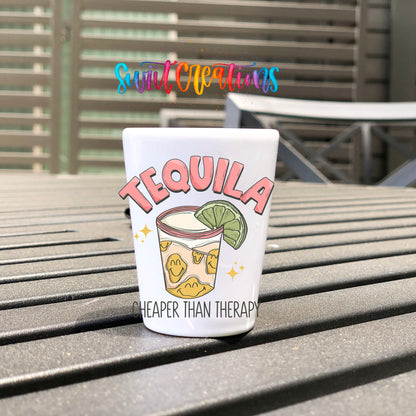 Tequila Cheaper Than Therapy UV DTF transfer on a white shot glass on an outdoor patio table