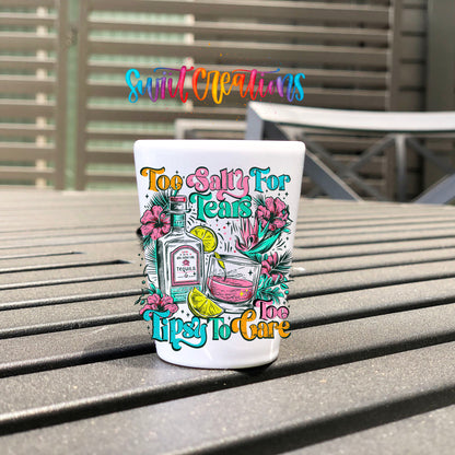 Too Salty For Tears Too Tipsy To Care UV DTF transfer on a white shot glass on an outdoor patio table