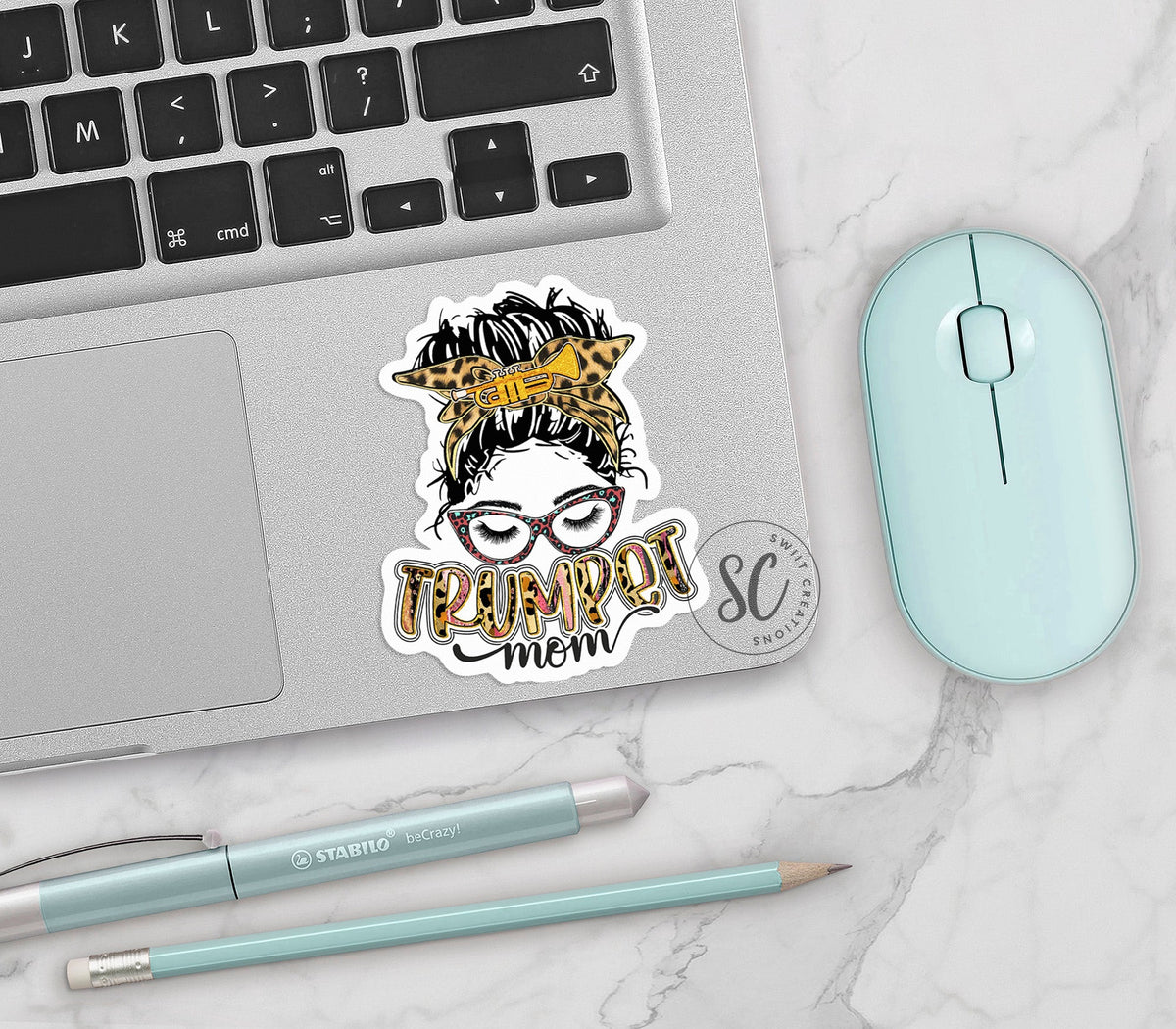 Trumpet Mom vinyl sticker on a silver laptop next to a mint mouse and pens