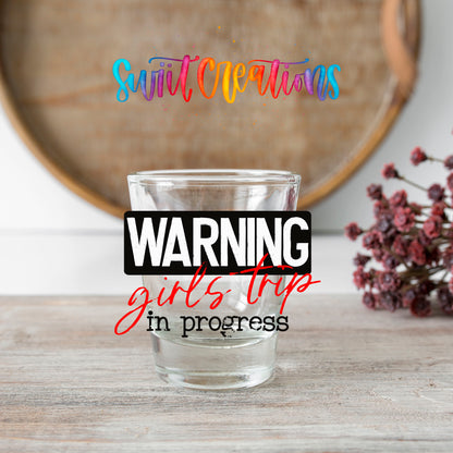 Warning Girls Trip in Progress shot glass transfer on a clear glass beside a wooden barrel and dried flowers