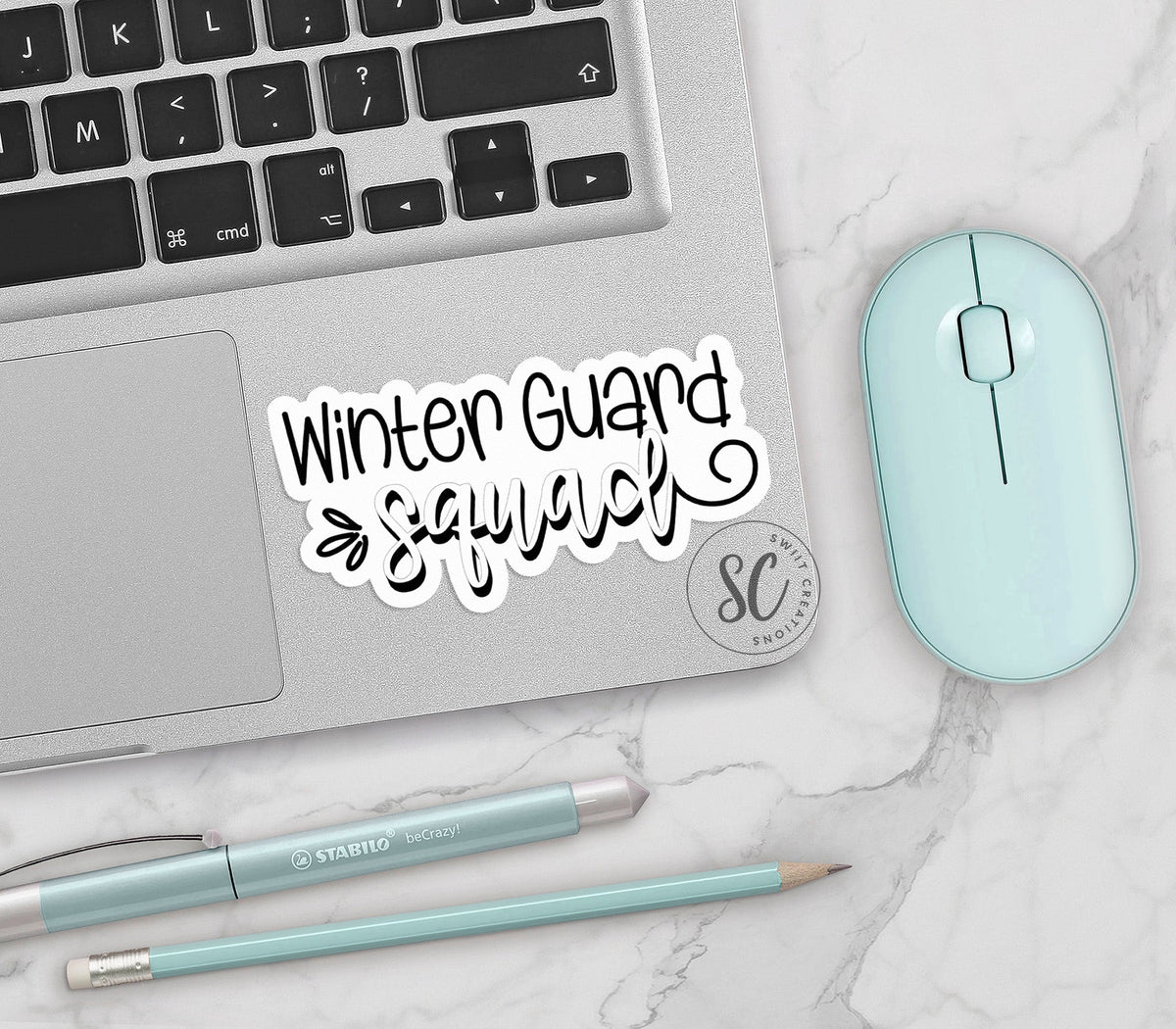 Winter Guard Squad vinyl sticker on a silver laptop next to a mint mouse and pens