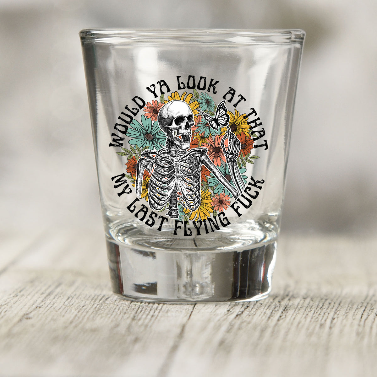 Would You Look At That My Last Flying F*ck shot glass UV DTF transfer with skeleton, butterfly, and wildflowers on a clear shot glass